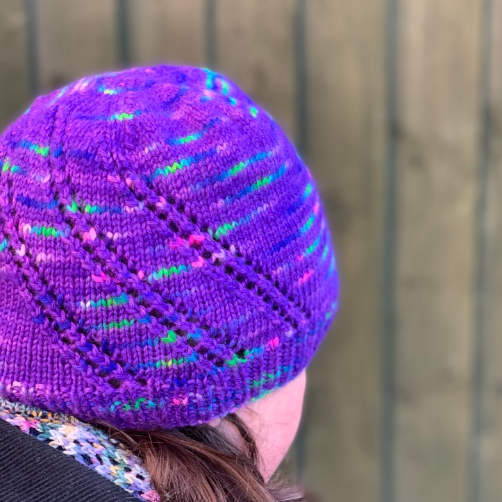 Northern Lights hat. Stocking stitch hat with 3 diagonal lace strips. Yarn used is purple with flashes of bright green, blue and pink.
