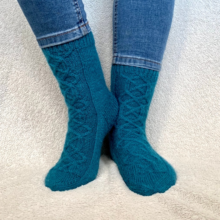 Borealis socks. Teal wool socks with cable detail running up the top of the foot and front of the leg.